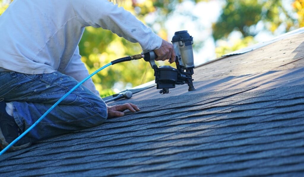using a nailgun to install new shingles on roof