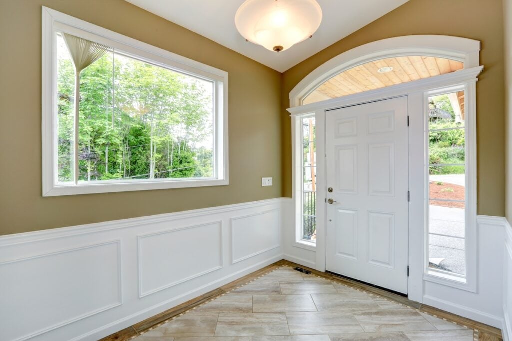 Entrance hallway with tile floor and beige wall with white trim. White door with arch and windows