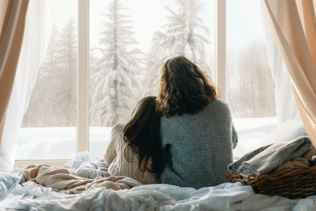 Happy loving family. Mother and daughter are hugging and enjoying winter nature in the window.