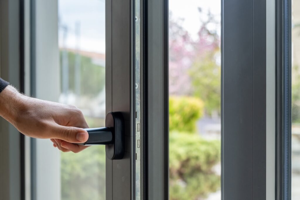 Male hand opens metal or PVC window closeup view. Man holding the aluminum door handle. Energy efficient, security frame profile, blur garden outdoor background