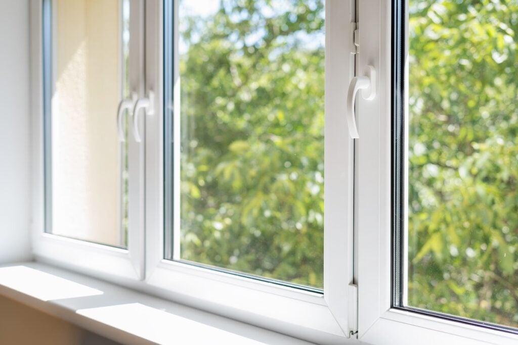 new plastic pvc window with white metal frame installed at modern house, view of blurred green trees.