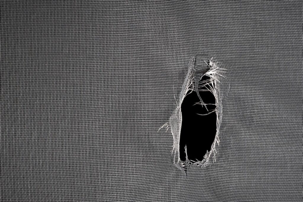 Window screen torn with a big hole against a black background.